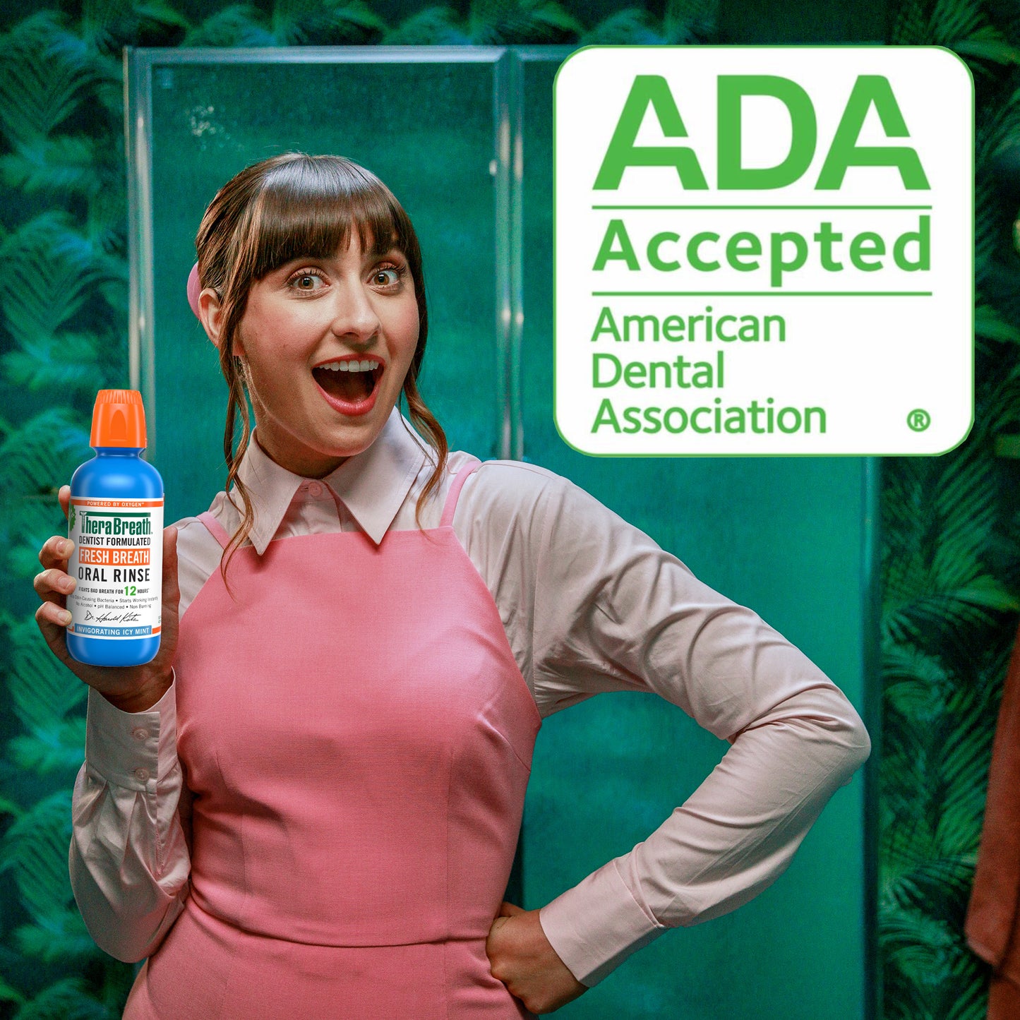 Woman smiling holding a bottle of TheraBreath Fresh Breath Oral Rinse Invigorating Icy Mint  - a sign says "ADA Accepted" showing that it is accepted by the American Dental Association 